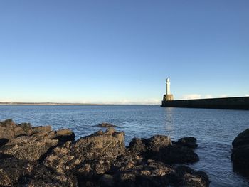 Lighthouse by sea against clear blue sky