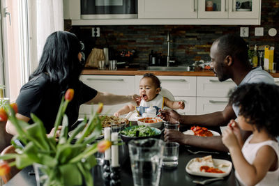 Mother feeding son sitting with family in kitchen