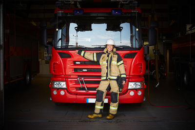 Full length portrait of smiling female firefighter standing in front of fire engine at fire station