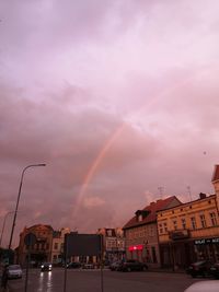 Rainbow over buildings in city at sunset