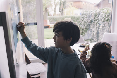 Boy drawing in living room while sister in background at home