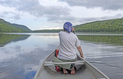 Rear view of man sitting on boat in lake against sky