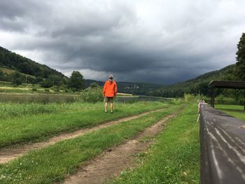Rear view of man on road amidst field against sky