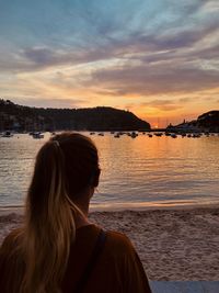 Rear view of woman looking at sea against sky during sunset