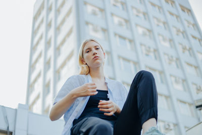 Low angle view of young woman sitting against building