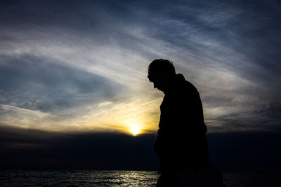 Silhouette man standing by sea against sky during sunset