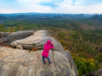 Woman taking photo of scenic mountain landscape. girl stay at tripod with camera