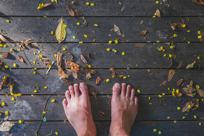 Low section of man standing by leaves on hardwood floor