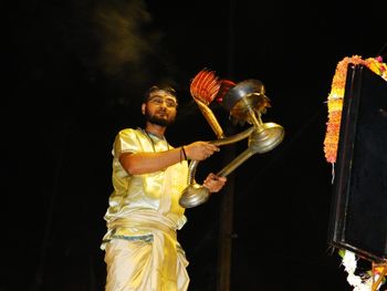 Low angle view of young man holding object while praying outdoors at night