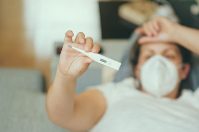 Woman holding thermometer lying down on bead at home