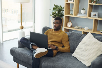 Young man using laptop while sitting on sofa at home