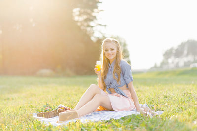 Beautiful young woman in a blue denim shirt and pink skirt in the garden at a picnic holding a glass