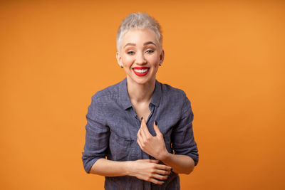 Portrait of happy young woman standing against orange background