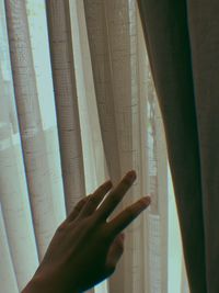 Cropped hand of woman holding curtain at home