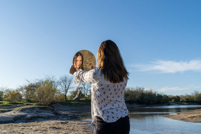 Low section of woman standing by water against sky