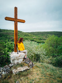 Woman sitting on wood against sky. women sitting near a catholic cross 