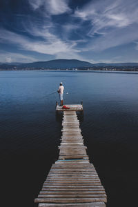 Man standing on pier over lake against sky