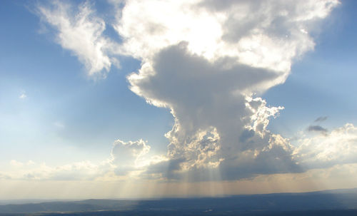 Low angle view of sunlight streaming through clouds over sea