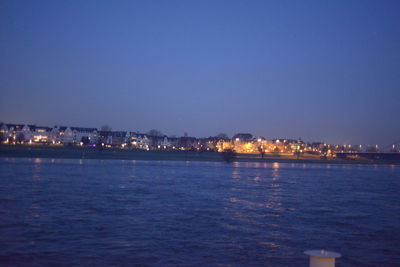 Illuminated city by sea against clear sky at night