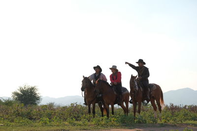 People riding horses on field against sky