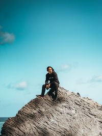 Man sitting on rock against blue sky