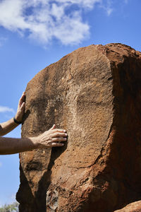 Low angle view of hand on rock against sky