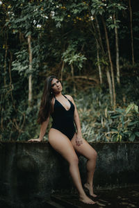 Side view of young woman sitting on land in forest