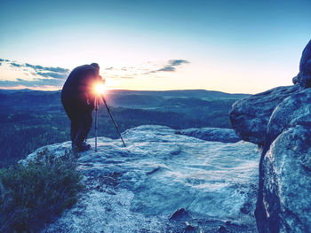 Amateur photographer takes photos with camera on tripod on rocky peak tourist in cold weather