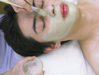 Cropped hands of massage therapist applying facial mask to man