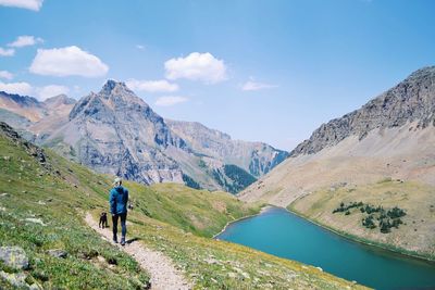 Rear view of woman with dog walking on mountain against sky