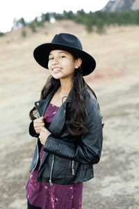 Portrait of young girl wearing a black fedora hat and black leather jacket in the mountains