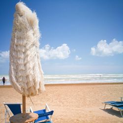 Parasol by lounge chairs at beach against blue sky