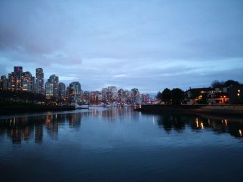 River by illuminated buildings against sky at dusk