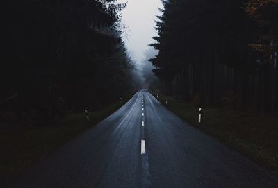 Empty road amidst trees against sky in forest