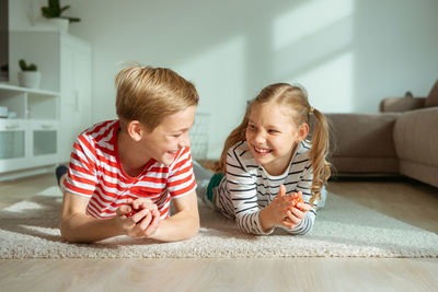 Cheerful siblings playing with dice while lying on carpet at home