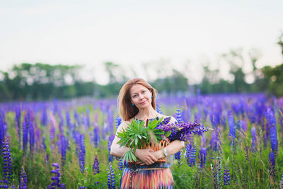 Young attractive woman holding a basket full of lupine flowers