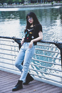 A young woman in punk style leans on a railing by the river