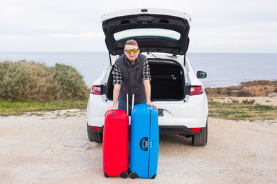 Portrait of camera standing by car on sea shore against sky