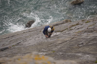 High angle view of man climbing rock by sea