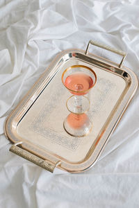 Rose wine in vintage gold-rimmed champagne coupe glass on silver tray on white bed sheets