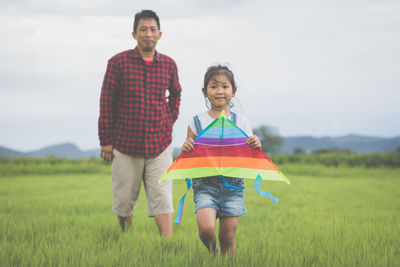 Portrait of girl with father holding kite while standing on grassy field