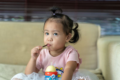 Thoughtful girl eating food while sitting against sofa at home