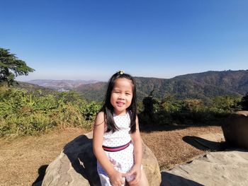Portrait of smiling girl sitting on mountain against clear sky
