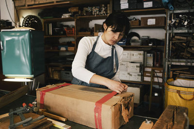 Female entrepreneur opening cardboard box in workshop