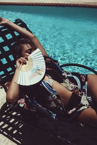 High angle view of woman relaxing on chair by swimming pool