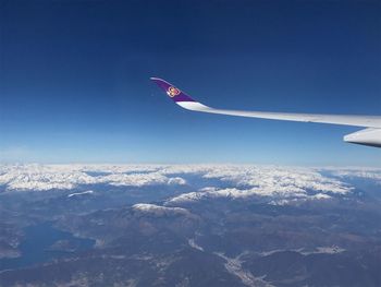 Airplane flying over snowcapped mountain against blue sky