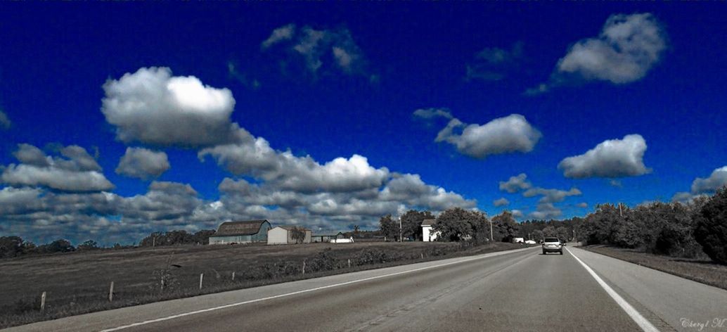 road, transportation, sky, the way forward, road marking, cloud - sky, blue, diminishing perspective, cloud, car, street, building exterior, vanishing point, architecture, built structure, empty, cloudy, land vehicle, country road, asphalt