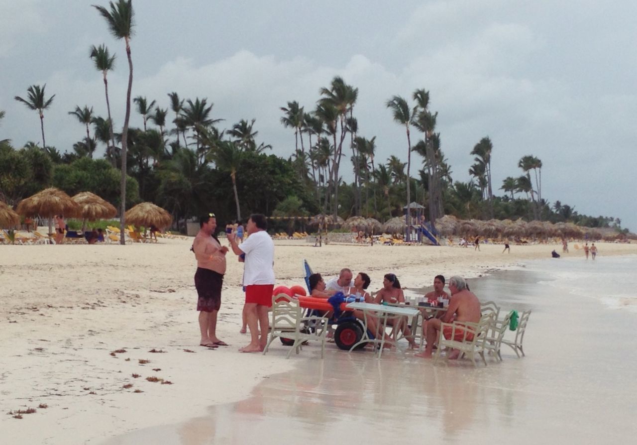 beach, sky, person, lifestyles, tree, sand, leisure activity, water, palm tree, men, sea, large group of people, vacations, shore, relaxation, cloud - sky, mixed age range, tourist, tourism