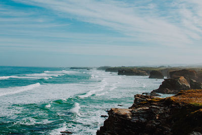 Scenic view of sea by rocky coastline against sky