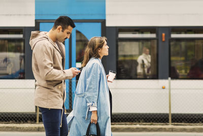 Side view of young man and woman standing at tram station